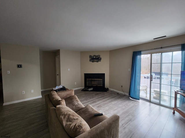 living room with baseboards, wood finished floors, visible vents, and a glass covered fireplace