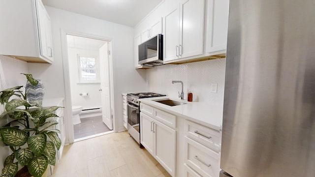 kitchen with a sink, light countertops, appliances with stainless steel finishes, white cabinets, and a baseboard radiator