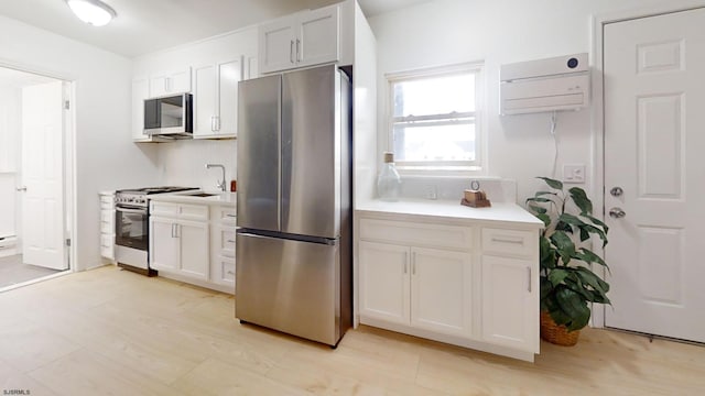 kitchen with a wall mounted air conditioner, light countertops, appliances with stainless steel finishes, white cabinets, and a sink