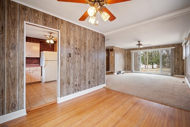 empty room with wooden walls, baseboards, light wood-type flooring, and a ceiling fan