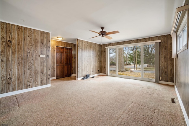 carpeted spare room featuring visible vents, baseboards, wood walls, and a ceiling fan