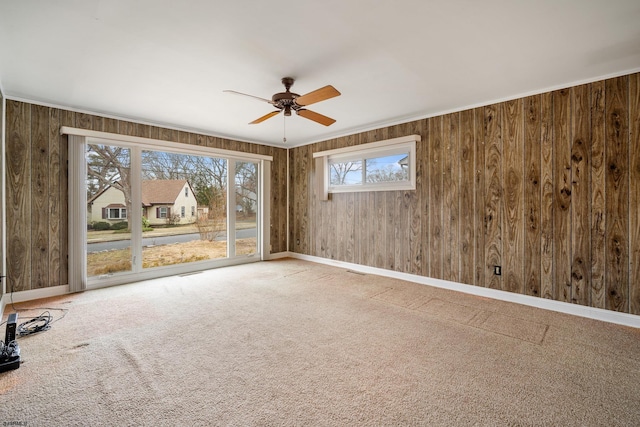 carpeted empty room with baseboards, ceiling fan, crown molding, and wood walls