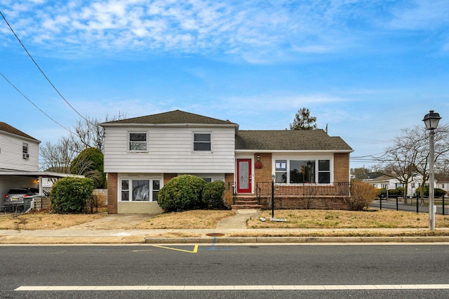 split level home with fence, brick siding, and roof with shingles