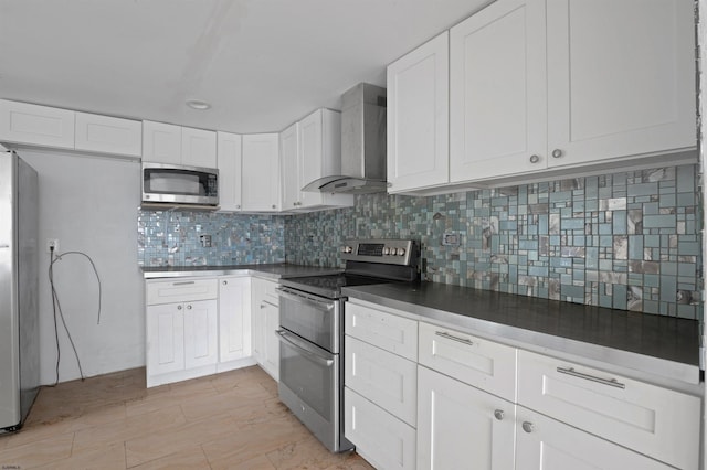 kitchen with tasteful backsplash, appliances with stainless steel finishes, white cabinets, and wall chimney range hood