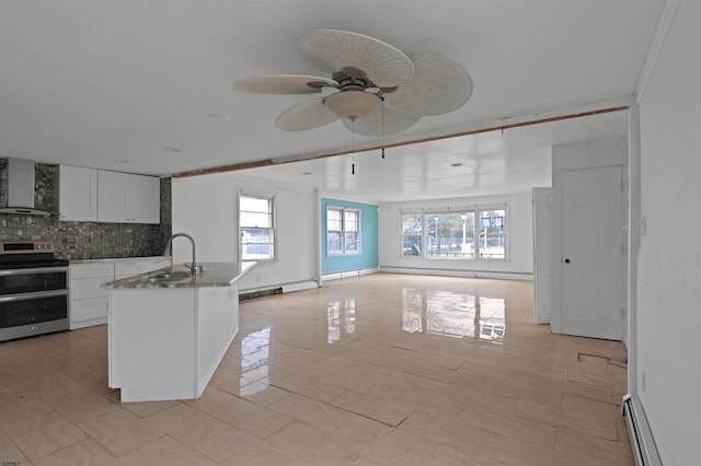 kitchen with tasteful backsplash, double oven range, baseboard heating, wall chimney exhaust hood, and a sink