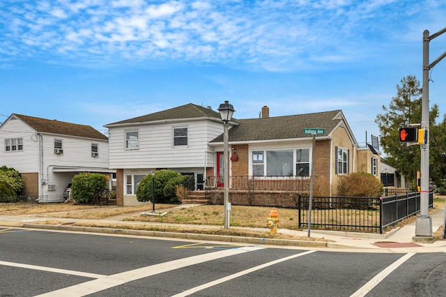 tri-level home with a fenced front yard, brick siding, a chimney, and a shingled roof