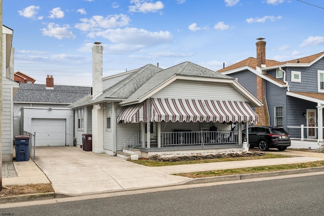 view of front facade featuring roof with shingles, a porch, an attached garage, a chimney, and concrete driveway