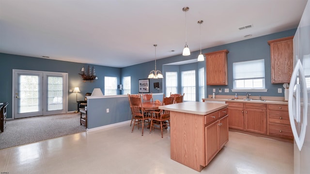 kitchen featuring a kitchen island, pendant lighting, light countertops, an inviting chandelier, and a sink