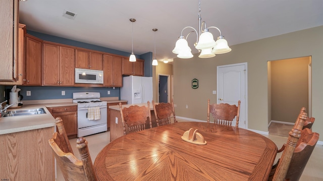 kitchen with a sink, white appliances, brown cabinetry, light countertops, and a chandelier