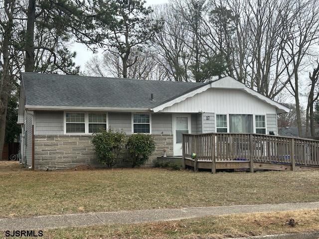 single story home featuring a wooden deck, stone siding, roof with shingles, and a front lawn