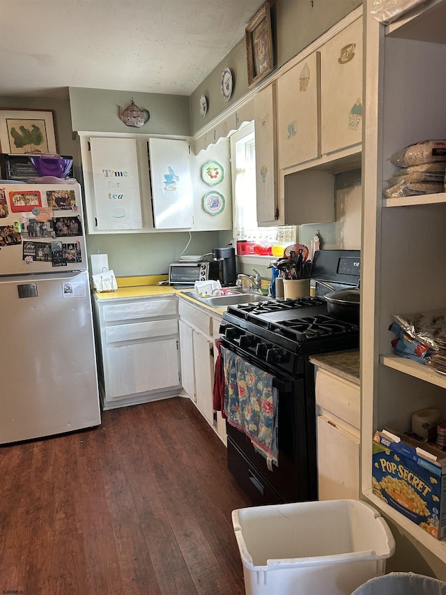 kitchen featuring black gas stove, dark wood-type flooring, light countertops, freestanding refrigerator, and a sink