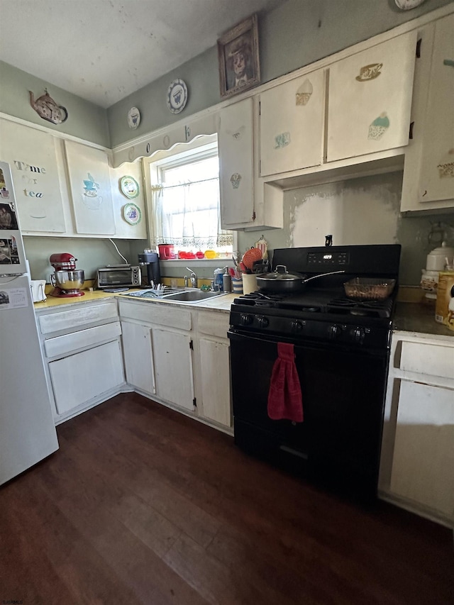 kitchen with black gas range oven, dark wood-style floors, light countertops, and freestanding refrigerator