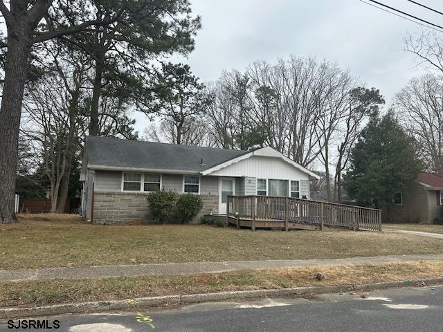 single story home featuring stone siding, a wooden deck, and a front yard