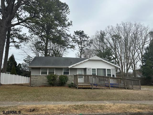 view of front of home with stone siding, a wooden deck, a front lawn, and fence