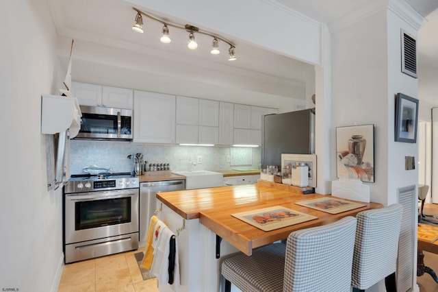 kitchen with tasteful backsplash, butcher block countertops, ornamental molding, stainless steel appliances, and white cabinetry