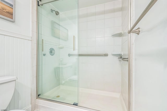 full bath featuring a wainscoted wall, toilet, and a stall shower