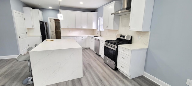 kitchen featuring a sink, a center island, appliances with stainless steel finishes, wall chimney range hood, and decorative backsplash