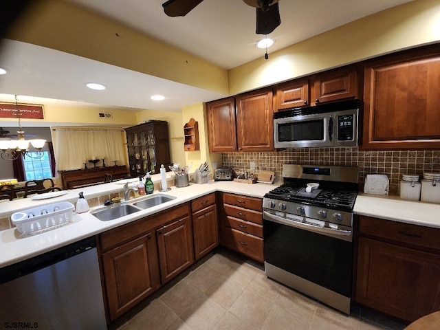 kitchen with a sink, decorative backsplash, light countertops, appliances with stainless steel finishes, and ceiling fan with notable chandelier