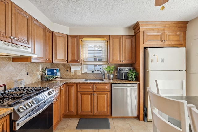 kitchen with under cabinet range hood, brown cabinets, appliances with stainless steel finishes, and a sink