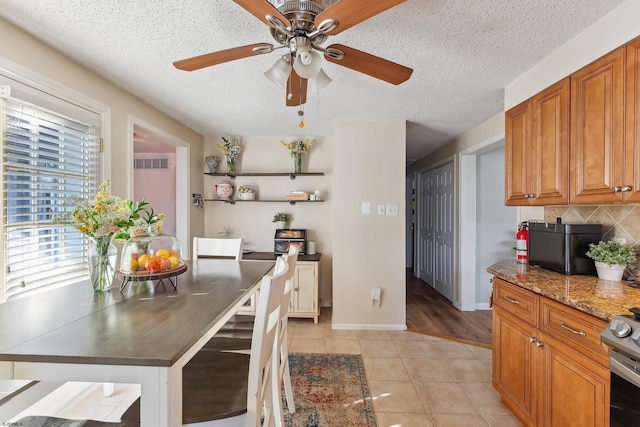 kitchen with a ceiling fan, brown cabinets, stainless steel electric stove, light tile patterned flooring, and tasteful backsplash