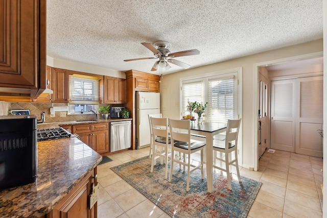 kitchen featuring freestanding refrigerator, a sink, ceiling fan, dishwasher, and brown cabinets