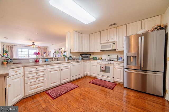 kitchen with white appliances, visible vents, light wood-style flooring, a sink, and white cabinets