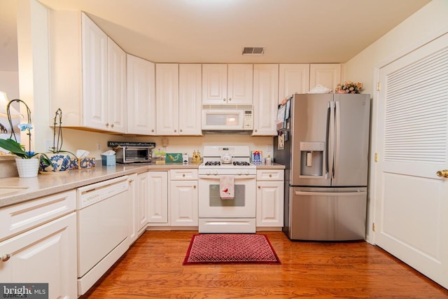 kitchen with visible vents, white cabinets, white appliances, and light wood-style floors