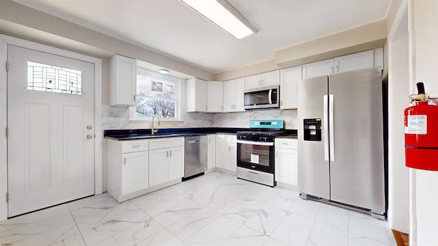 kitchen featuring a sink, appliances with stainless steel finishes, dark countertops, marble finish floor, and backsplash