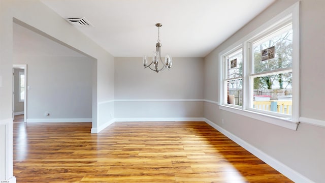 spare room featuring a notable chandelier, visible vents, light wood finished floors, and baseboards