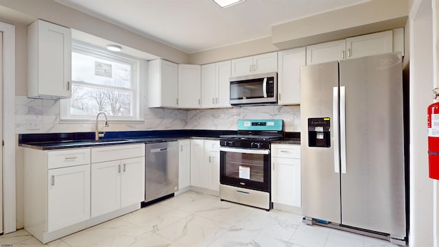 kitchen with a sink, appliances with stainless steel finishes, white cabinetry, dark countertops, and marble finish floor