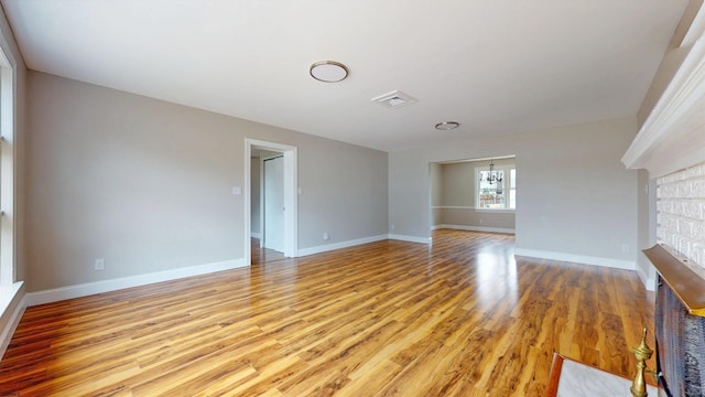 unfurnished living room with visible vents, baseboards, an inviting chandelier, and light wood-style flooring