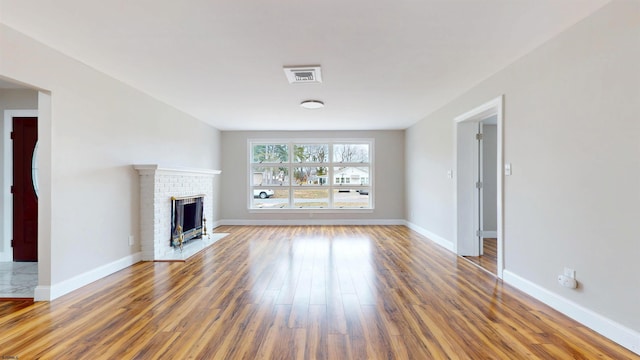 unfurnished living room featuring visible vents, a fireplace, baseboards, and wood finished floors