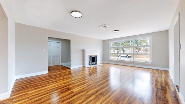 unfurnished living room featuring visible vents, baseboards, a brick fireplace, and wood finished floors