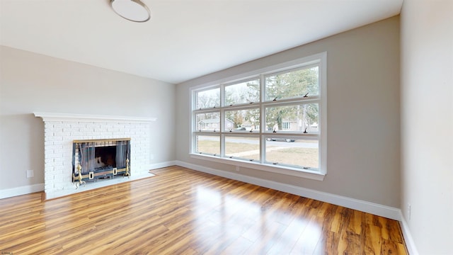 unfurnished living room featuring baseboards, plenty of natural light, a brick fireplace, and wood finished floors