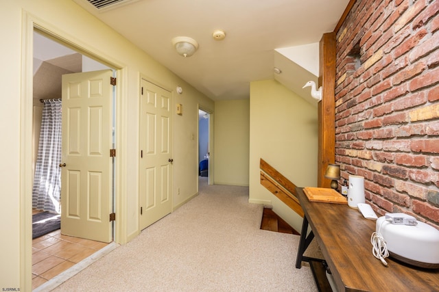 corridor featuring tile patterned flooring, brick wall, baseboards, and carpet