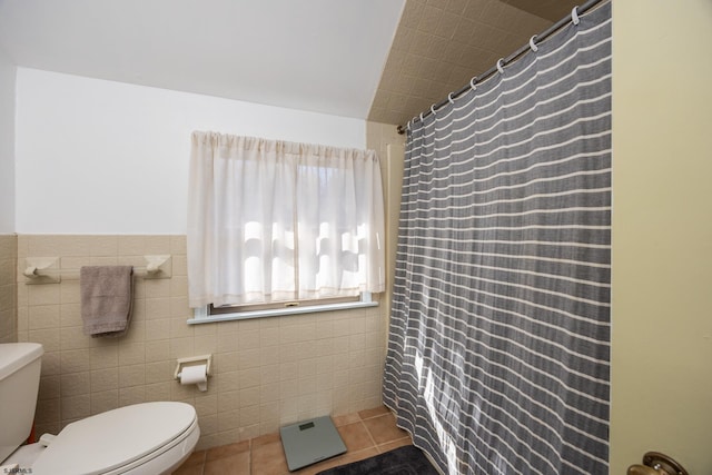 full bath featuring curtained shower, toilet, wainscoting, tile patterned floors, and tile walls