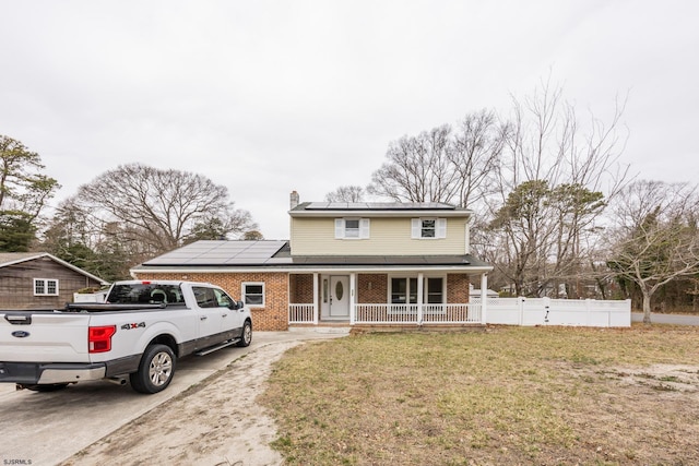 traditional-style house with brick siding, a porch, concrete driveway, roof mounted solar panels, and a chimney