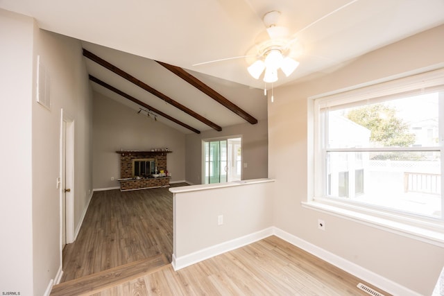 spare room featuring a brick fireplace, vaulted ceiling with beams, baseboards, wood finished floors, and a ceiling fan