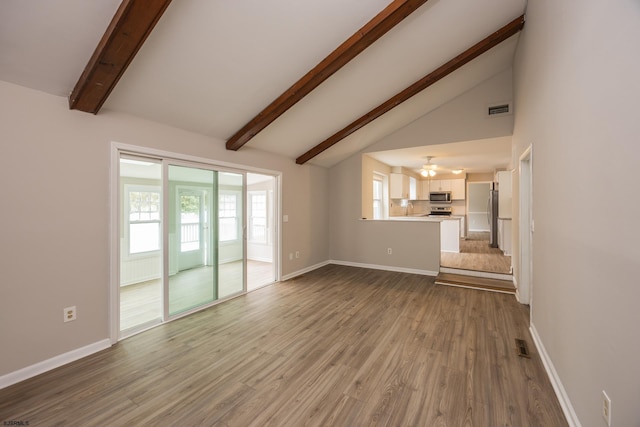 unfurnished living room featuring beam ceiling, visible vents, plenty of natural light, and wood finished floors