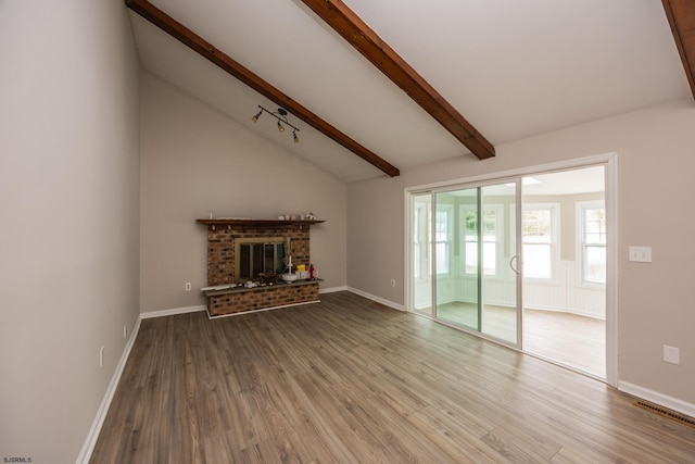 unfurnished living room with baseboards, a brick fireplace, wood finished floors, and vaulted ceiling with beams