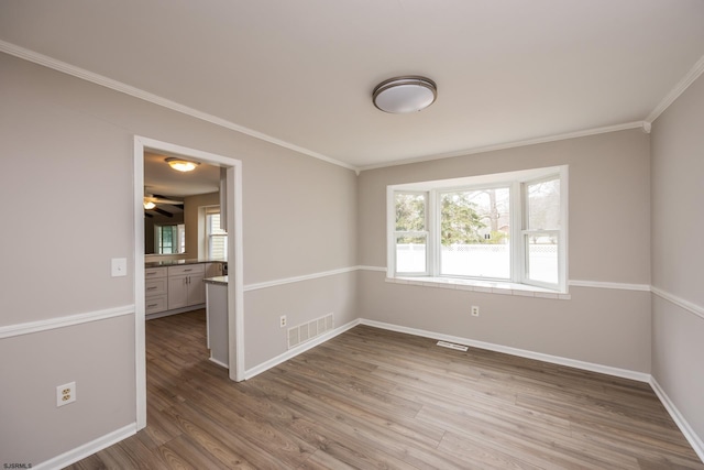 spare room with crown molding, wood finished floors, visible vents, and baseboards