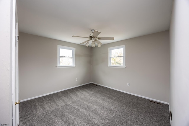 spare room featuring a wealth of natural light, dark colored carpet, baseboards, and ceiling fan