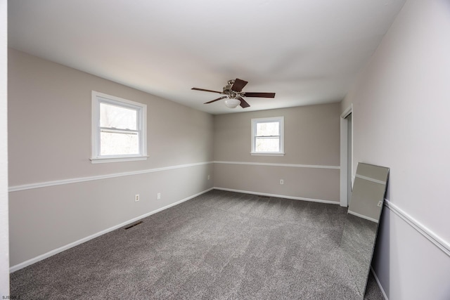 spare room featuring visible vents, dark carpet, baseboards, and a ceiling fan