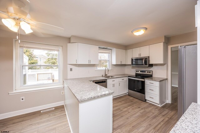 kitchen with a sink, light wood-style floors, a peninsula, appliances with stainless steel finishes, and white cabinets