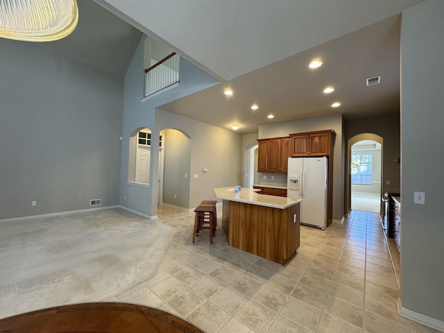 kitchen with brown cabinets, a center island, arched walkways, white fridge with ice dispenser, and light countertops