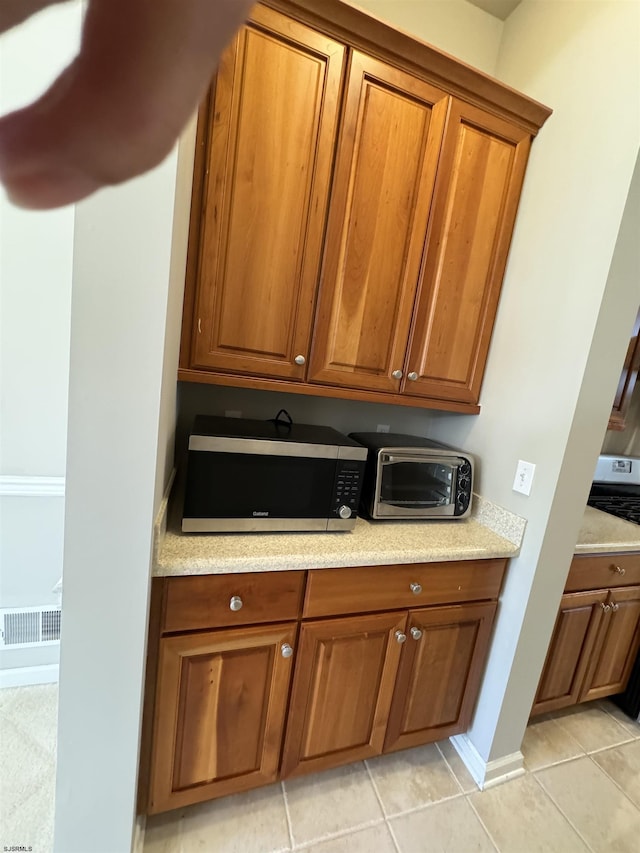 kitchen with stainless steel microwave, a toaster, brown cabinets, and light tile patterned floors