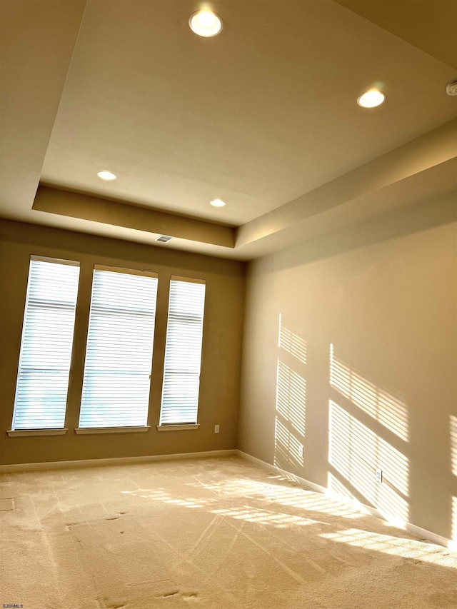 spare room with a raised ceiling, recessed lighting, baseboards, and light carpet