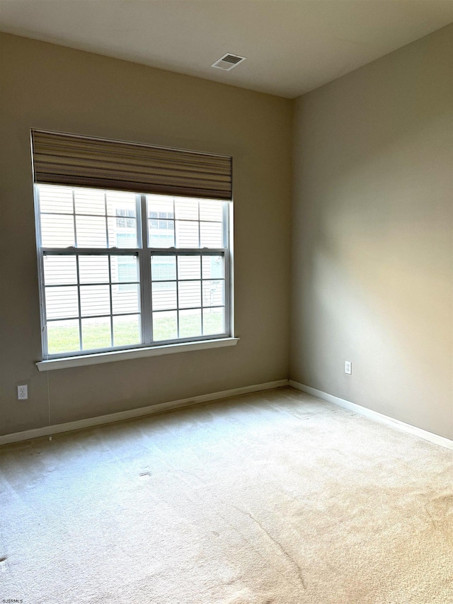 carpeted empty room featuring baseboards, visible vents, and a wealth of natural light