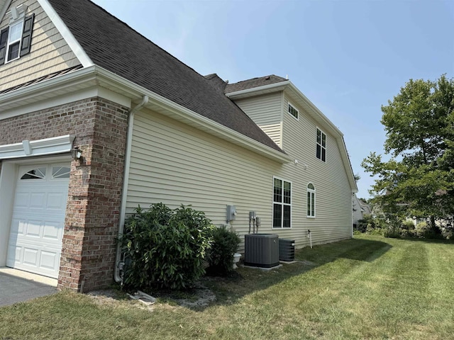 view of side of home featuring cooling unit, a lawn, roof with shingles, and brick siding