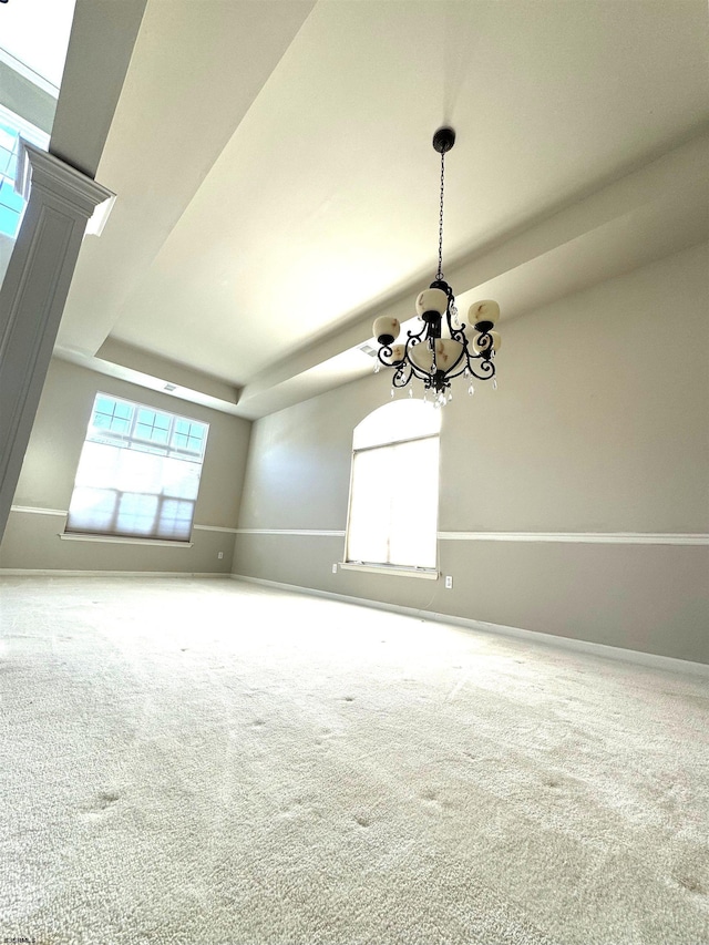 spare room featuring a notable chandelier, a healthy amount of sunlight, a tray ceiling, and carpet floors